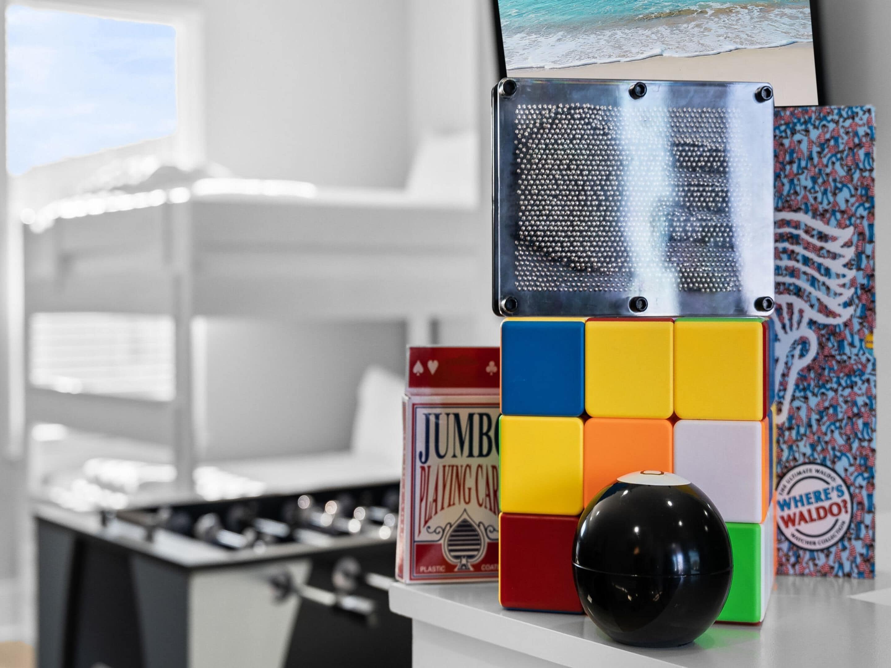 A kitchen counter with a Rubik's Cube, a black spherical object, and a book titled 'Jumbo Playing Cards'.