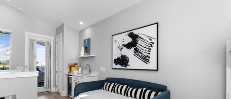 Ein modernes Wohnzimmer mit einem blauen Sofa, einer Küchenzeile inklusive Spüle und Schränken sowie einem großen abstrakten Gemälde an der Wand.