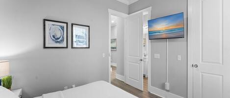 Un dormitorio con una cama grande, un televisor instalado en la pared y una puerta que da a un baño.