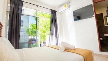 A hotel room with a bed, a window with curtains, a TV, and an air conditioning unit.