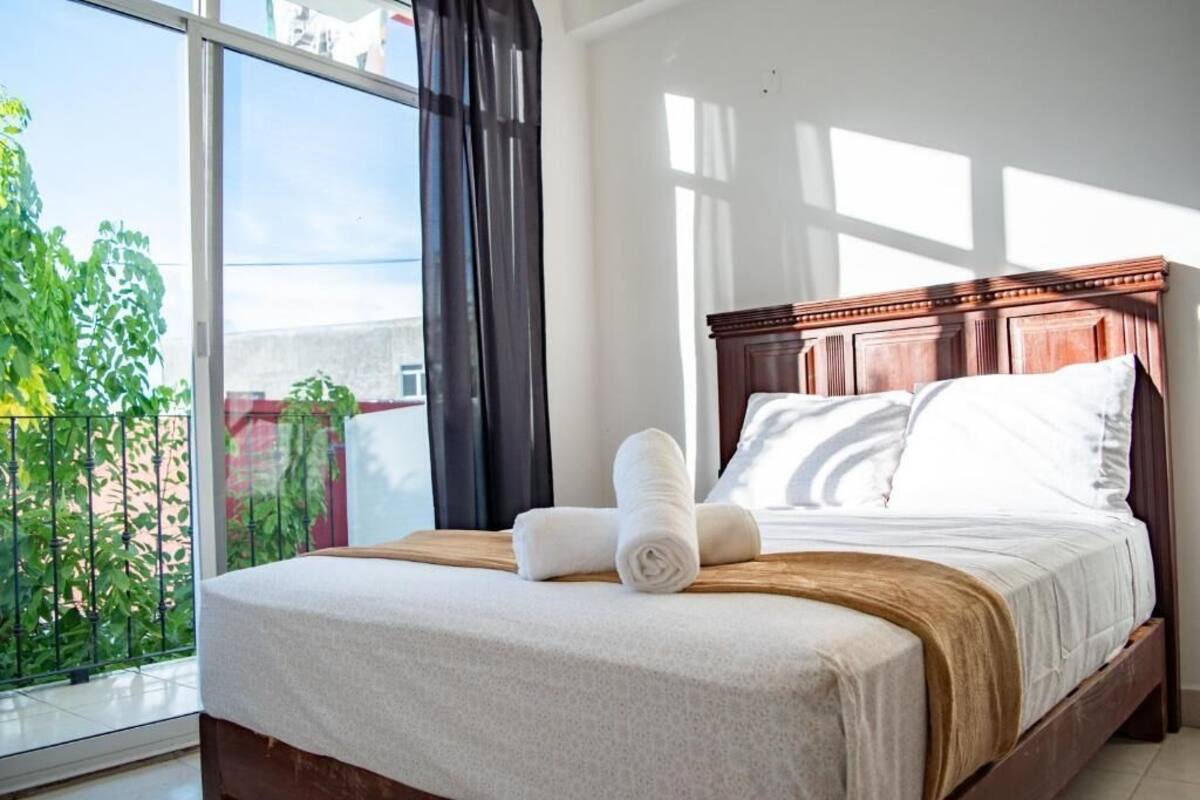 A hotel room with a large window, a wooden bed, and a view of greenery outside.