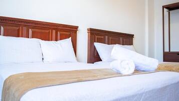 Habitación de hotel con dos camas, cada una con cabeceros de madera, ropa de cama blanca y una toalla enrollada sobre la cama.
