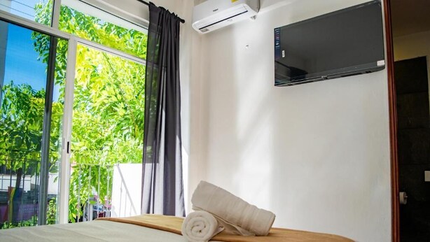 Habitación de hotel con cama, televisor montado en la pared y ventana con cortinas.