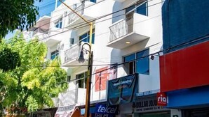 Un edificio de varios pisos con balcones, una señal visible de 'Neto' y diversas tiendas, incluyendo 'Telcel' y 'Dollar Juju'.
