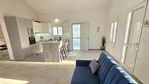 Amplia sala de estar con un sofá azul, una cocina al fondo e iluminación colgante.