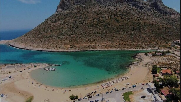 Una zona costera con playa, barcos y una montaña.