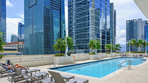 A rooftop pool area with lounge chairs and palm trees, surrounded by high-rise buildings. - Brickell Bay 3304 (Miami)