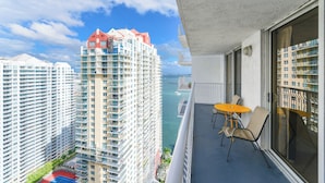 A balcony with a table and chairs, overlooking a cityscape with high-rise buildings and a body of water. - Brickell Bay 3304 (Miami)