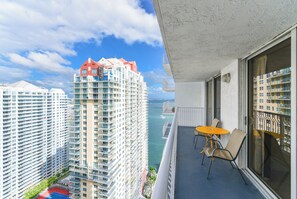 A balcony with a table and chairs, overlooking a cityscape with high-rise buildings and a body of water. - Brickell Bay 3304 (Miami)