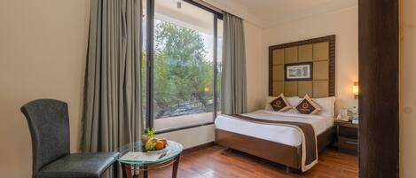 Habitación de hotel con cama, una silla, una mesita con fruta, ventana con cortinas y ventilador de techo.