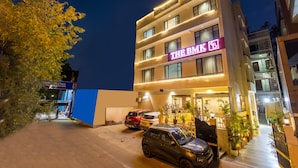 Ein mehrstöckiges Hotel mit Neonreklame, parkenden Autos und Blumentöpfen.