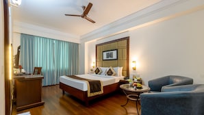 Ein Hotelzimmer mit Bett, Schreibtisch, Stuhl, Nachttisch mit Lampe und Deckenventilator.