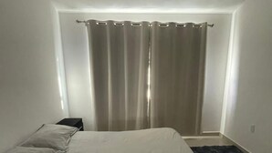 A bedroom with a bed, a window with curtains, and a dark carpet. - MillenniumIII - Bed/Matrimonial - Shared Bathroom and/or SofaBed - PET Friendly (Santiago de Querétaro)