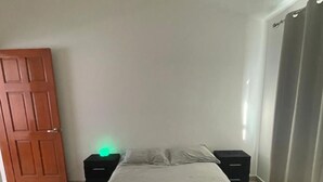 A bedroom with a bed, two bedside tables, a door, and a window with curtains. - MillenniumIII - Bed/Matrimonial - Shared Bathroom and/or SofaBed - PET Friendly (Santiago de Querétaro)