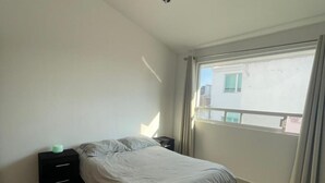 A bedroom with a bed, a nightstand, a window with curtains, and a view of buildings outside. - MillenniumIII - Bed/Matrimonial - Shared Bathroom and/or SofaBed - PET Friendly (Santiago de Querétaro)