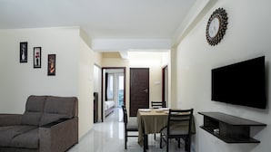 A modern living room with a sofa, dining table, chairs, and a flat-screen TV mounted on the wall.