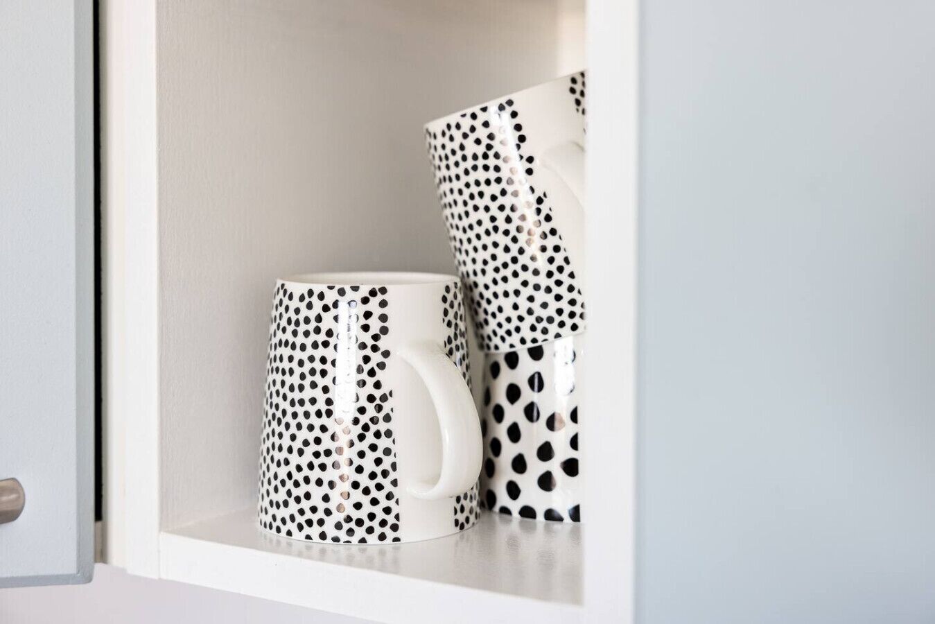 A white cabinet with two white mugs featuring black polka dot patterns.