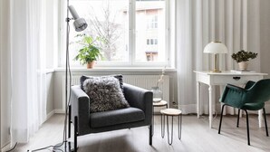Una sala de estar moderna con un sofá gris, una mesita redonda pequeña, un escritorio con una silla y una lámpara de pie.