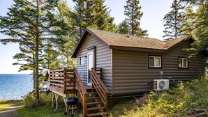 A cabin with a wooden deck, a staircase, and an air conditioning unit.