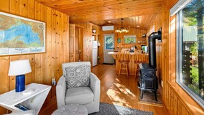 A cozy cabin interior with a wooden ceiling, a map on the wall, a dining area with a stove, and a comfortable seating area.