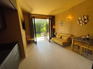 Una sala de estar moderna con un sofá, mesa de comedor y sillas. Hay un televisor a la izquierda y una ventana con cortinas.