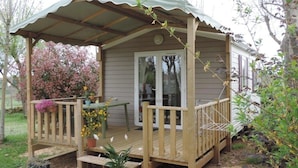 A wooden deck with a covered porch, a table, and potted plants. - ZEcamping 3 étoiles animé toboggans mobil-home 22m2 2 pers (Chateauroux)