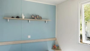 A bedroom with a bed, two pillows, a window, and wall-mounted shelves with decorative items. - ZEcamping 3 étoiles animé toboggans mobil-home 22m2 2 pers (Chateauroux)