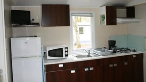 A compact kitchen with a refrigerator, microwave, sink, and stove. - ZEcamping 3 étoiles toboggans dog friendly animations mobil-home TV (Chateauroux)