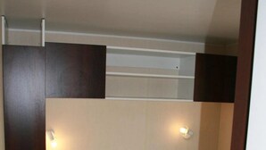 A compact, single-bed room with a wooden wardrobe and two wall-mounted light fixtures. - ZEcamping 3 étoiles toboggans dog friendly animations mobil-home TV (Chateauroux)