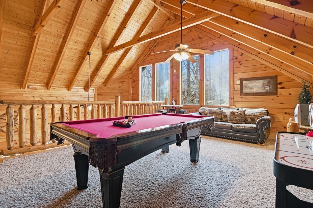 A wooden interior with a pool table, a sofa, and a ceiling fan.