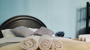 A neatly made bed with rolled towels, a dark headboard, and a blue wall.