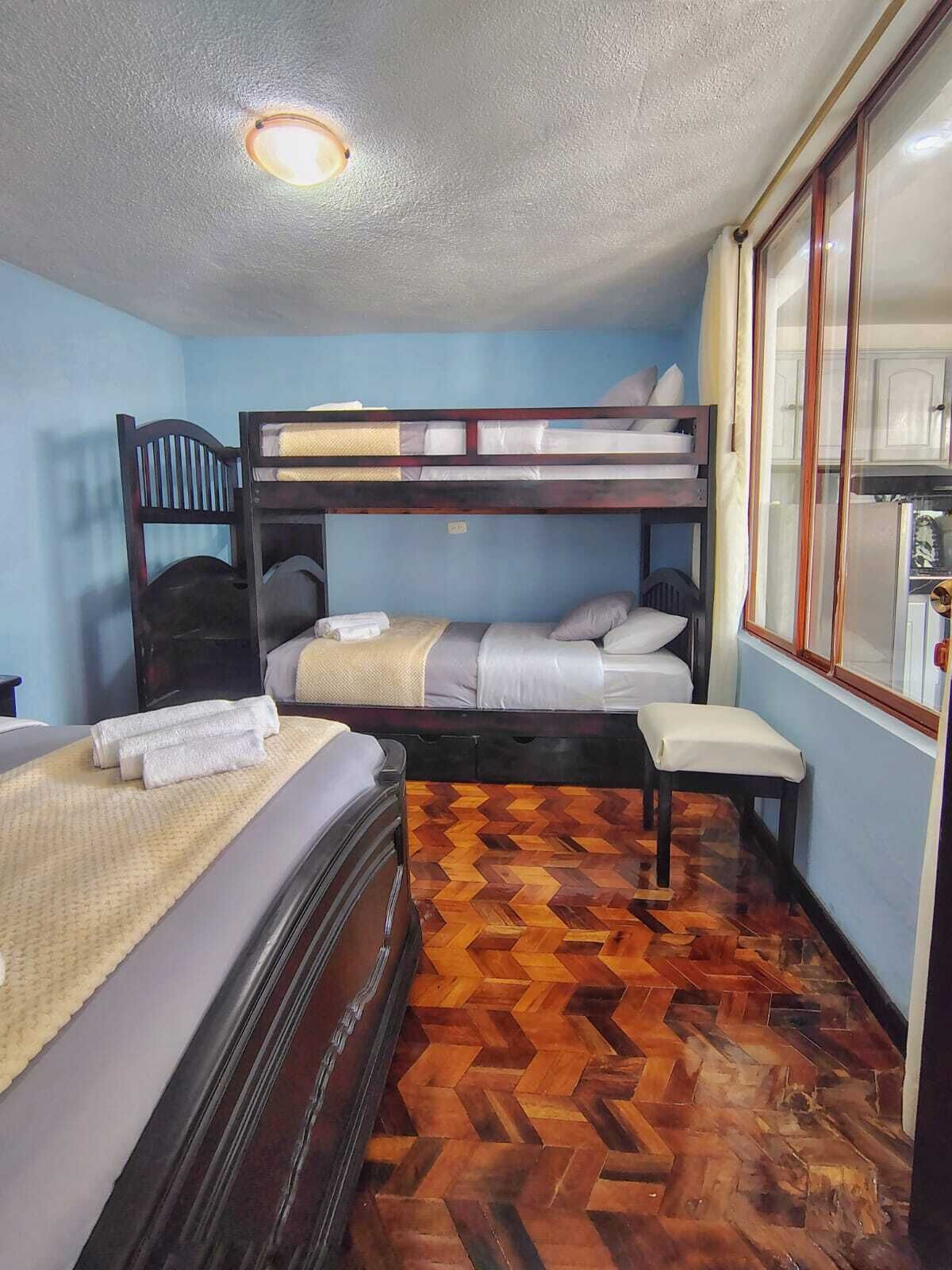 A room with a bunk bed, a single bed, and a wooden floor.