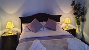 A neatly made bed with pillows, two bedside lamps, and rolled towels on a headboard.