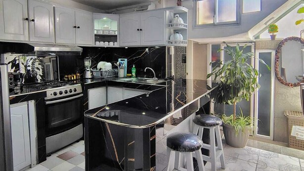 A modern kitchen with a black marble island, white cabinets, and a bar area with stools.