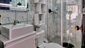 A modern bathroom with a marble backsplash, a white sink, a toilet, and a glass-enclosed shower area.