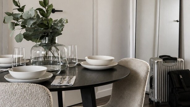 A dining area with a round table, chairs, a vase with greenery, and a large mirror on the wall. - Borg Katariinankulma | Design Apt · Balcony With View · Free Parking (Pori)