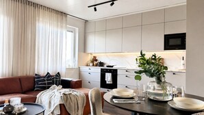 A modern living room with a sofa, a coffee table, and a dining area with a table set for two. - Borg Katariinankulma | Design Apt · Balcony With View · Free Parking (Pori)