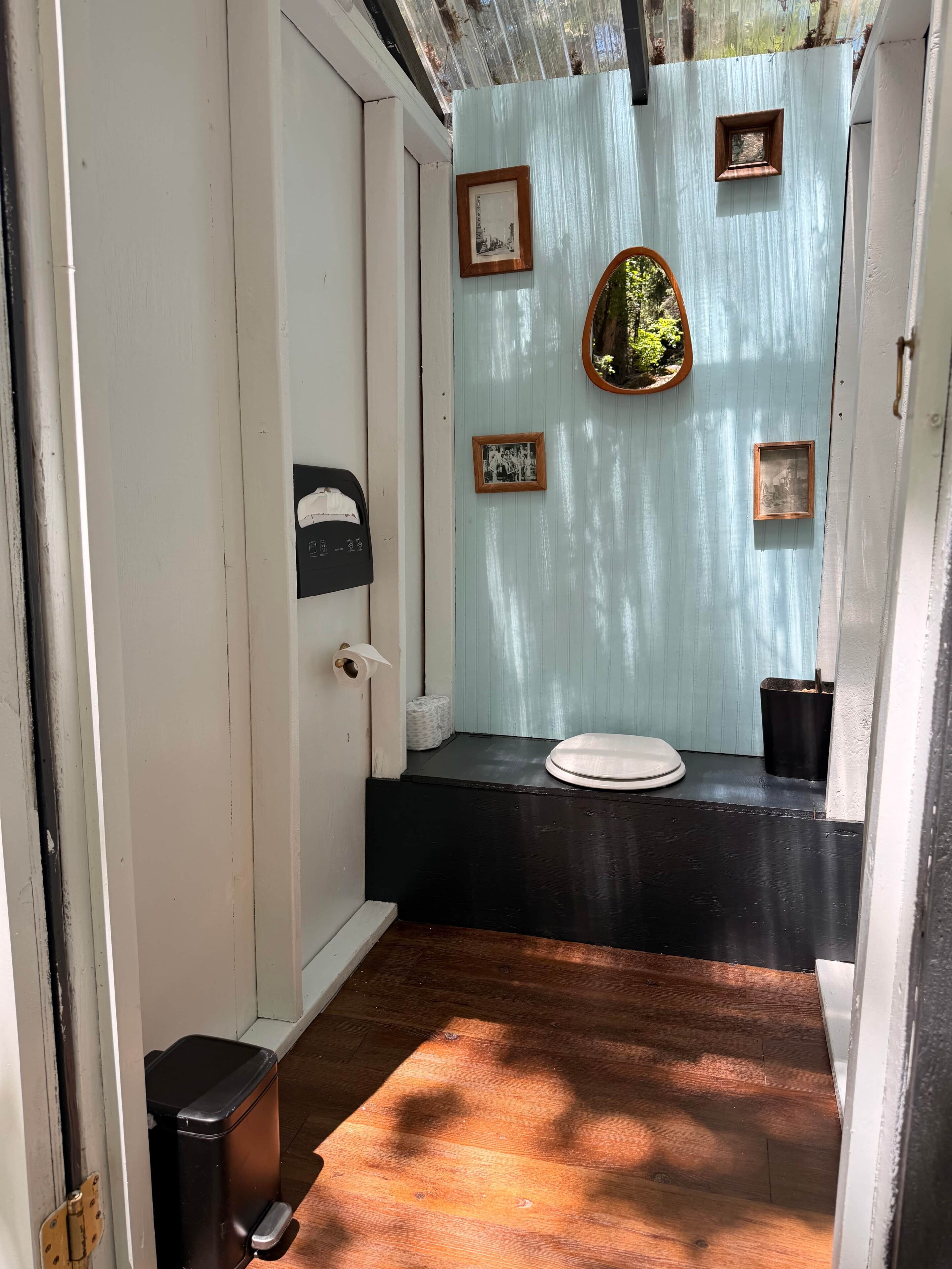A narrow hallway leading to a bathroom with a toilet, a trash bin, and framed pictures on the wall.