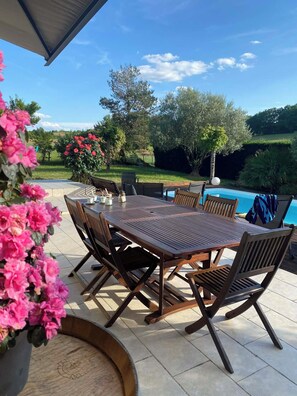 Une terrasse extérieure avec une table et des chaises en bois, une piscine et un jardin fleuri.