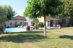 Un bâtiment en pierre doté d’une piscine, d’un espace extérieur aménagé pour s’asseoir et d’un arbre au premier plan.