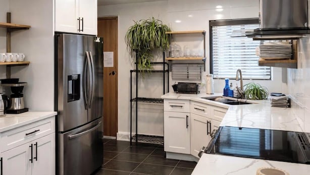 Una cocina moderna con armarios blancos, un refrigerador de acero inoxidable, una estufa negra y un lavamanos.