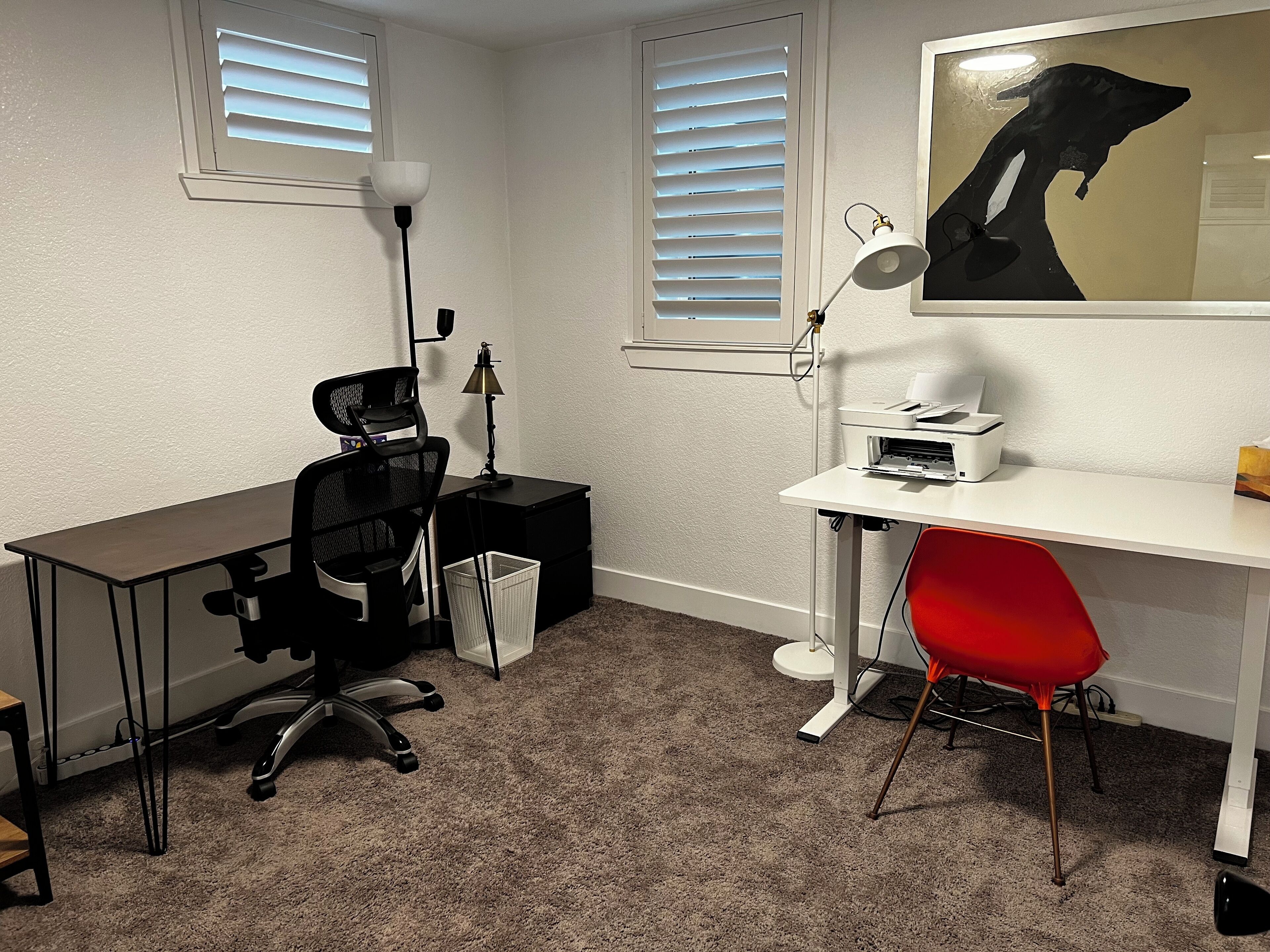 A small office with a desk, chair, printer, and a lamp.