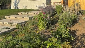 Una casa de una sola planta con fachada de ladrillo, un porche delantero y un jardín bien cuidado con diversas plantas y flores.