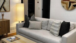 Una sala de estar moderna con un sofá gris, una mesa de centro de madera, una lámpara y una obra de arte en la pared.