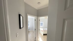 A hallway leading to a bedroom with a bed, a door, and a framed picture on the wall.