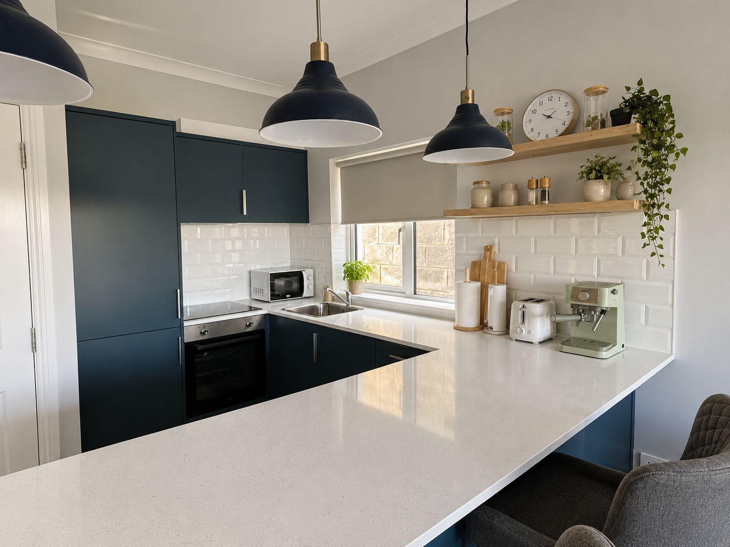 A modern kitchen with dark cabinets, a white countertop, a microwave, a coffee machine, and pendant lighting.