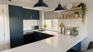 A modern kitchen with dark cabinets, a white countertop, a microwave, a coffee machine, and pendant lighting.