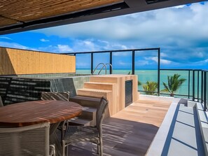 A modern outdoor terrace with a wooden table and chairs, a small pool, and a view of the ocean. - Beachfront Gourmet Studio with Private Pool (João Pessoa)