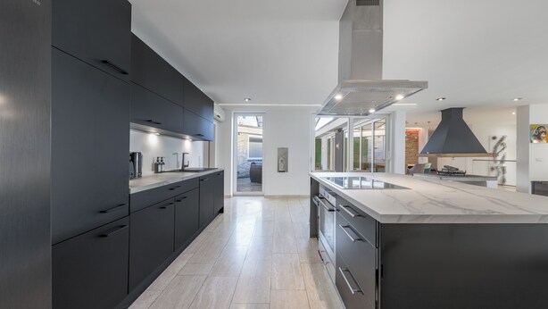 Una cocina moderna con armarios oscuros, una isla grande y vistas al comedor.