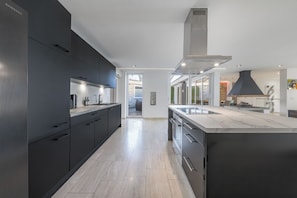 A modern kitchen with dark cabinetry, a large island, and a view to the dining area. - Luxury bungalow with heated private pool, sauna & discreet and central location. (Düsseldorf)